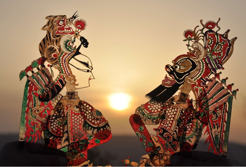 Two ornate Chinese shadow-puppet figures face each other against a glowing sunset.